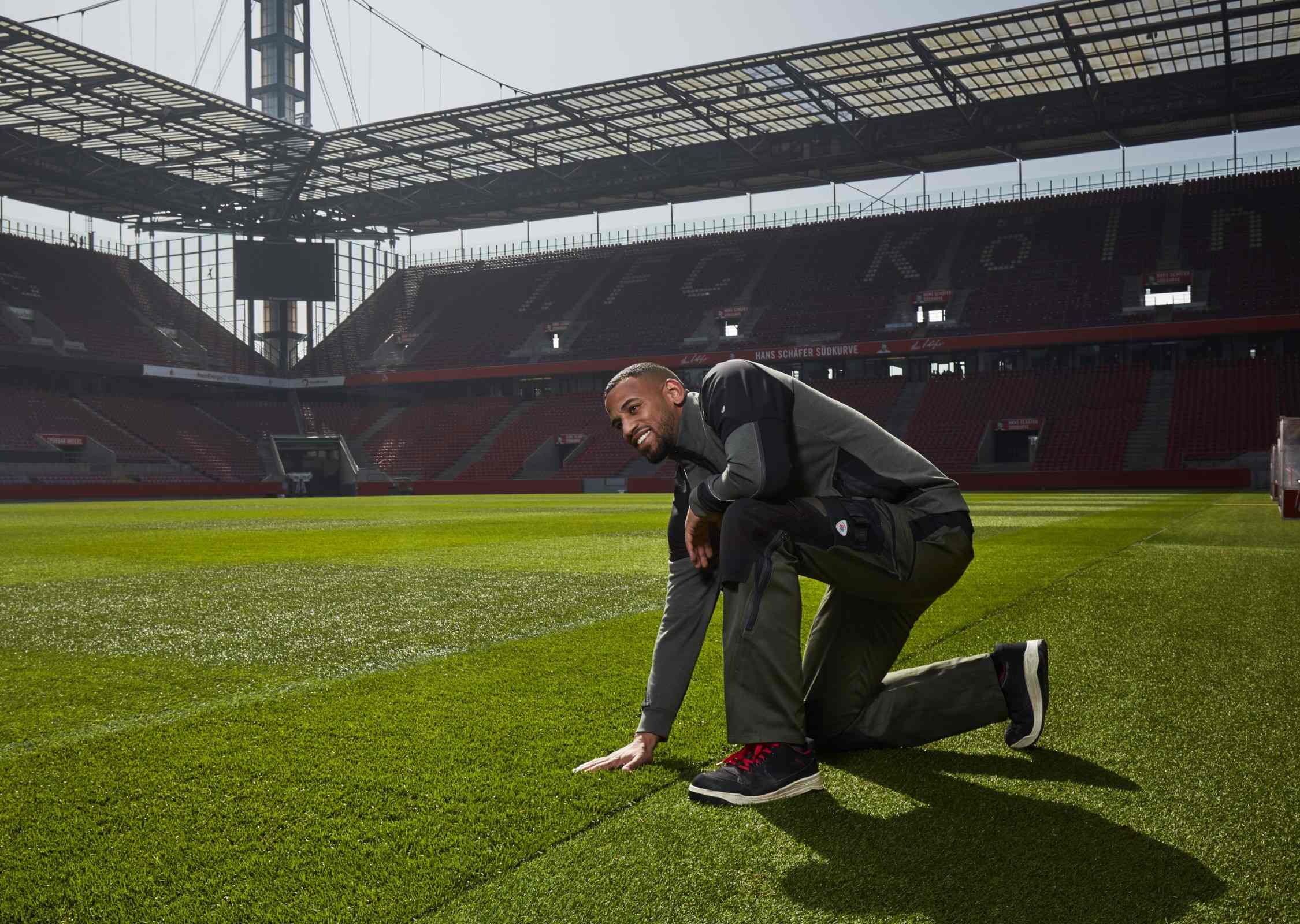 Greenkeeper im Rheinenergiestadion trägt BP® Arbeitskleidung und fasst den Rasen an.