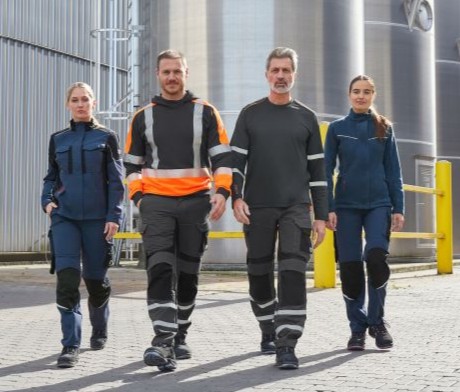 Team aus Frauen und Männern vor Industriegebäude in Multinorm-Warnschutzkleidung.