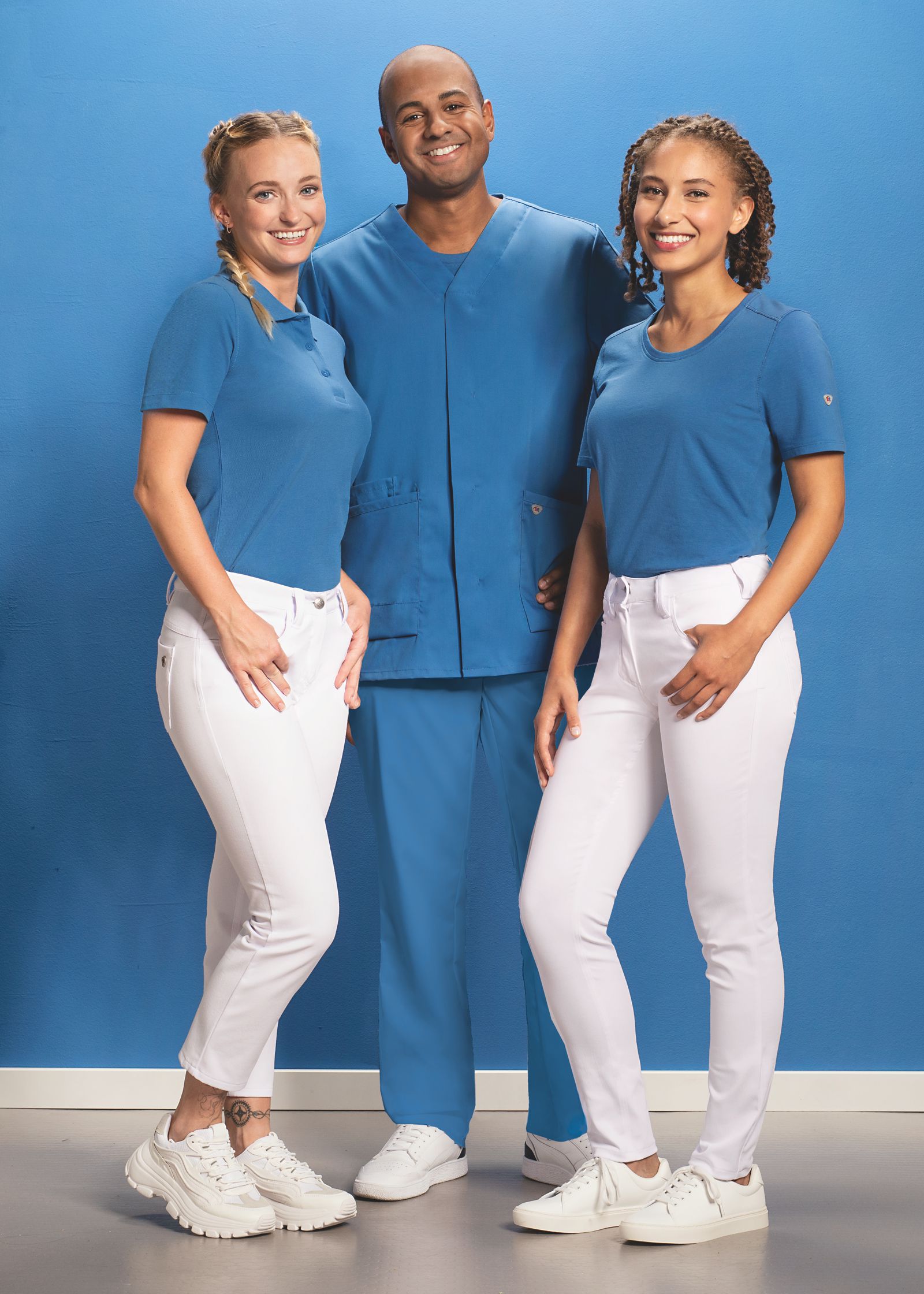 Drei Pfleger*innen posieren in hellblauen Pflege-Outfits.