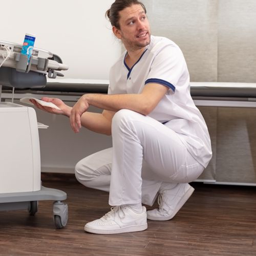 Un infirmier est en position couchée et porte un pantalon de travail blanc et une casaque.