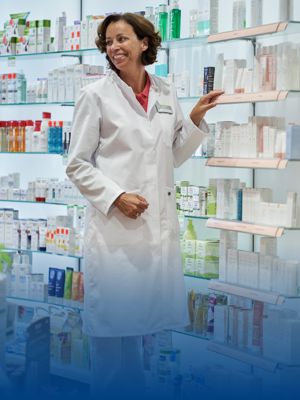 Eine Apothekerin in weißer Arbeitskleidung steht neben dem Medikamentenregal.