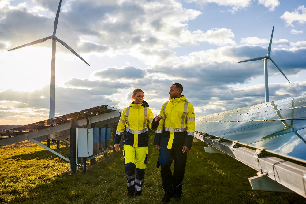 Un homme et une femme traversent une installation solaire en vêtements de signalisation Multinorm jaune fluo.
