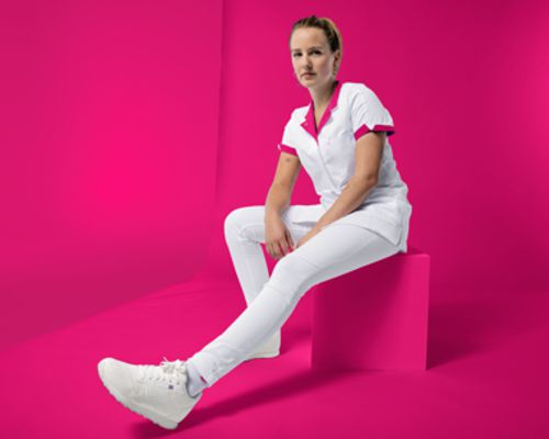 Une aide-soignante porte un pantalon blanc et une casaque blanche et rose.