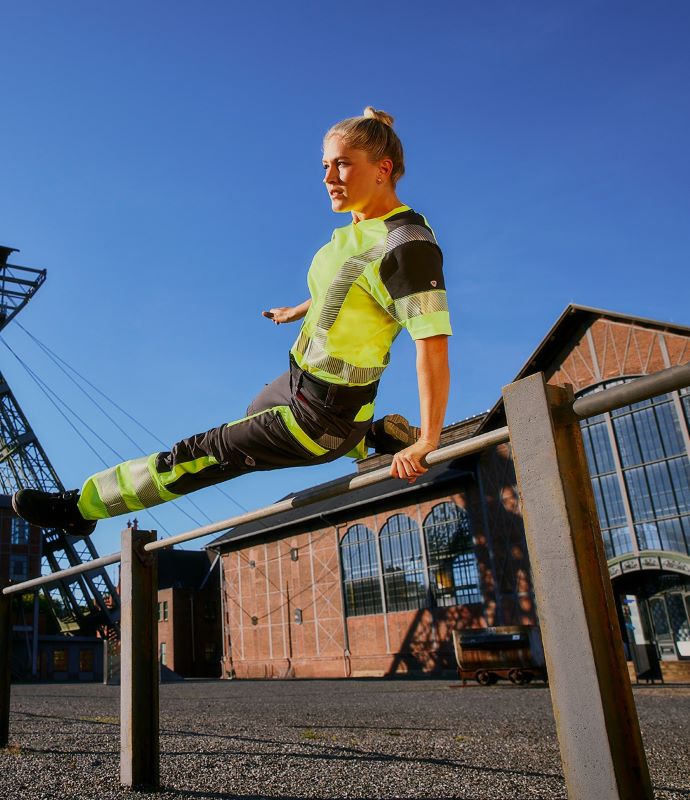 A woman wearing high-visibility clothing for women jumps over a pole.