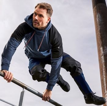 Ein Mann in einer hybriden und flexiblen Arbeitshose springt über eine Stange.