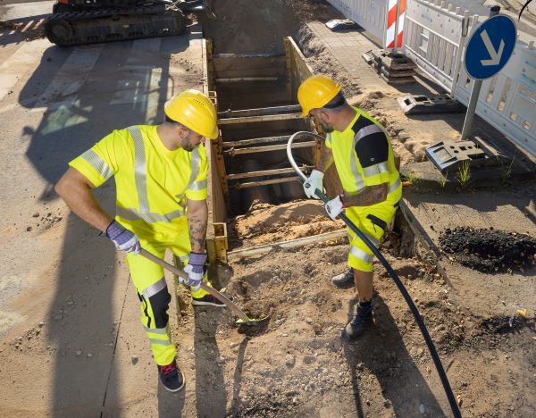 Zwei Bauarbeiter im Strassenbau arbeiten bei Hitze in Arbeitskleidung mit UV-Schutz.