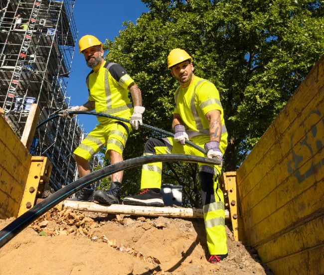 Deux constructeurs de routes posent un câble en tenue de signalisation.