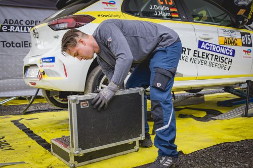 Automechaniker in Schutzkleidung führt Reparaturarbeiten bei E-Rennauto durch.