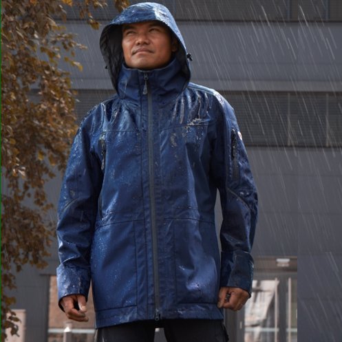 Mann in regenjacke mit Kapuze in strömendem Regen
