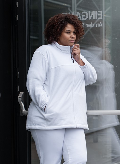 Woman in a white fleece jacket stands in front of a doorway.