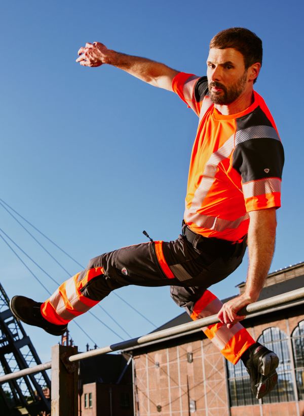 Ein Mann in hivis Arbeitskleidung in orange springt über eine Stange.