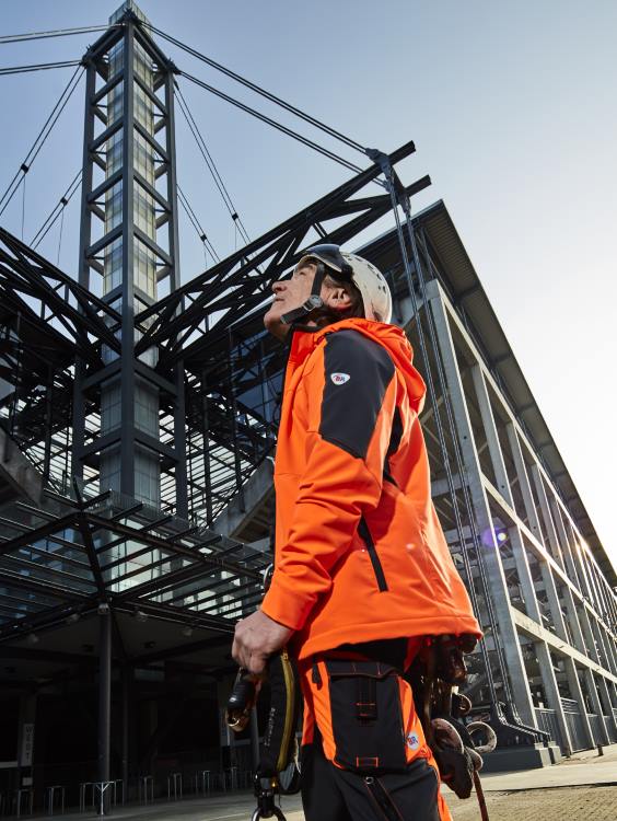 Ein Gebäudereiniger in BP® Arbeitskleidung schaut auf ein Gebäude hoch.