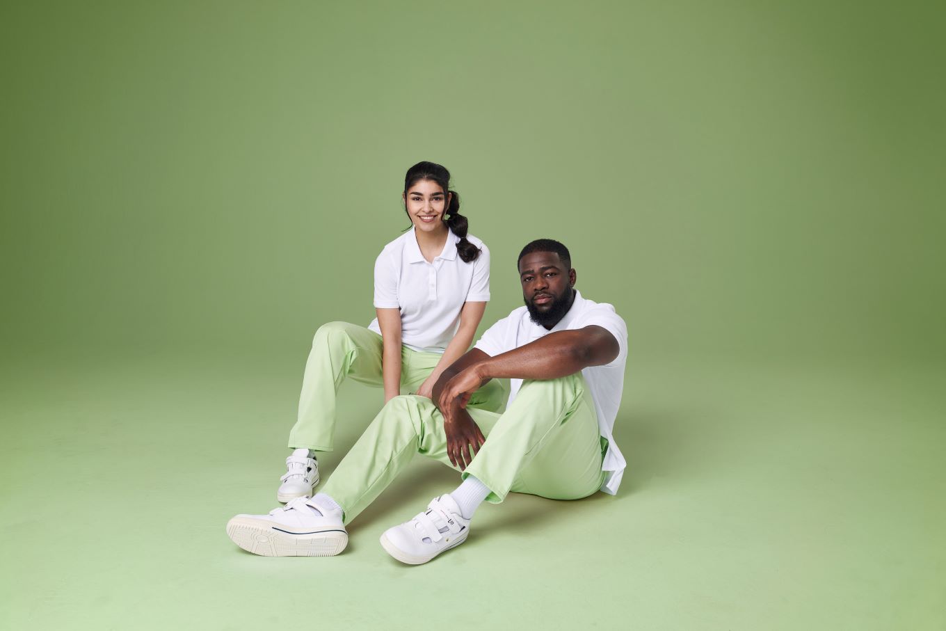 Ein Pfleger und eine Pflegerin tragen Arbeitskleidung in weiß grün.