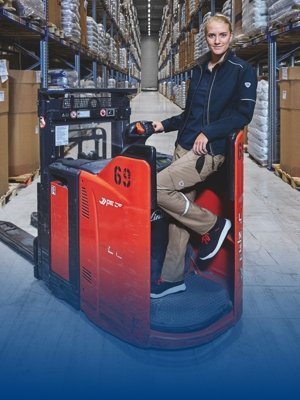 Employee in work clothes standing on a forklift truck in a warehouse.