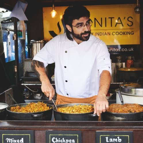 Een mannelijke streetfoodkok draagt een witte koksjas in zijn foodtruck.