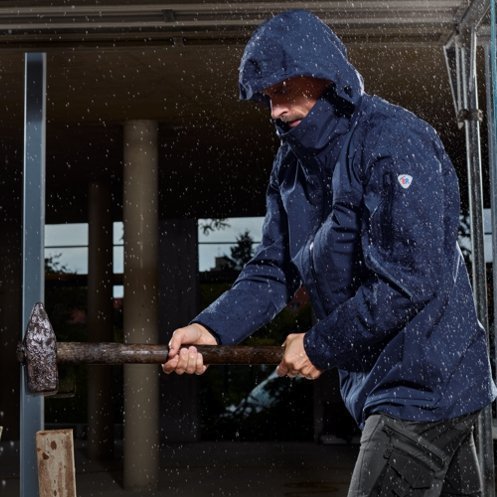 A man wears a BP® workwear rain jacket and hammers in rainy weather.