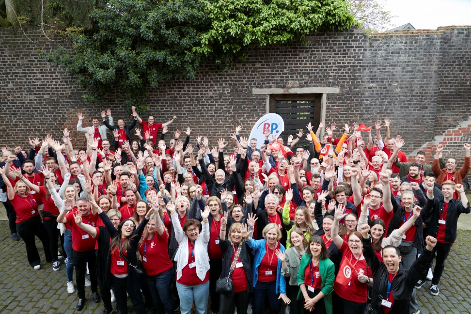 Around 100 BP® employees raise their hands in the air at a company event.