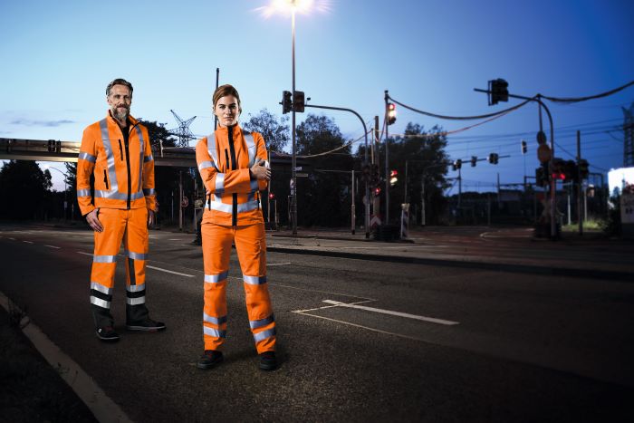 Ein Bauarbeiter und eine Bauarbeiterin stehen auf einer Straße und tragen Hivis Arbeitskleidung.