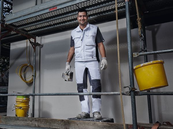 Ein Maler steht in Arbeitskleidung auf einem Gerüst.