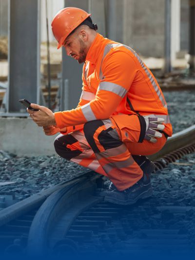 Gleisarbeiter hockt auf einem Gleis in BProtected Arbeitskleidung.