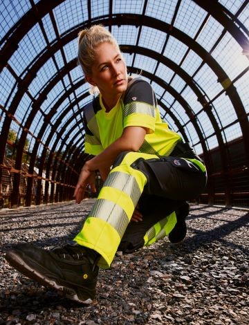 Eine Frau in der Hocke mit gelber hivis Kleidung für Damen.