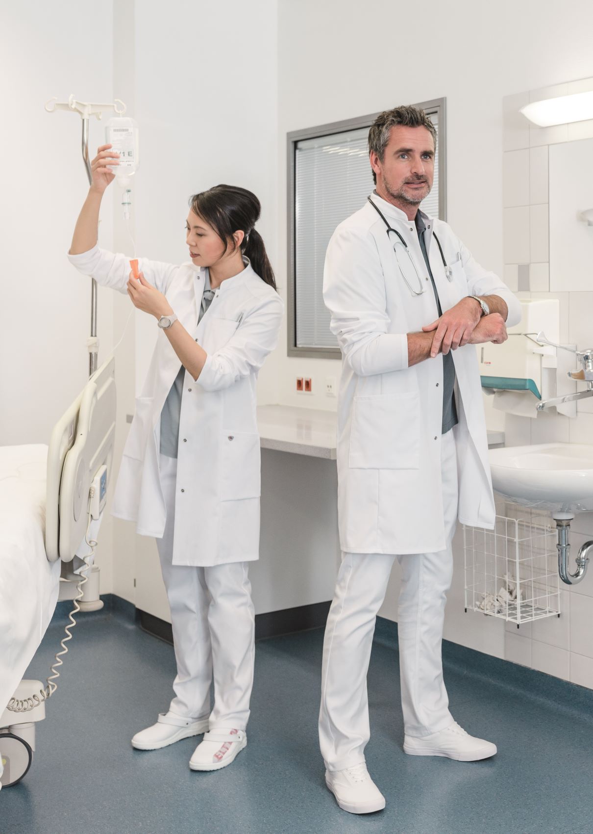 Eine Mann und eine Frau stehen mit weißer Klinikbekleidung in einem Raum der Klinik.