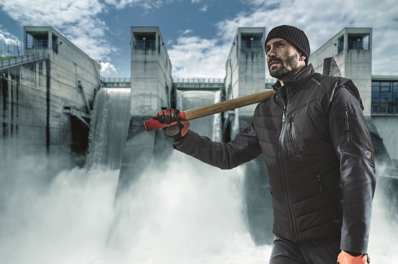 Craftsman in a dark-coloured work waistcoat with a sledgehammer in front of a dam.