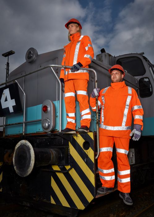 Een spoorwegmedewerker en een vrouwelijke spoorwegmedewerker staan op een spoorweg en dragen oranje opvallende kleding.