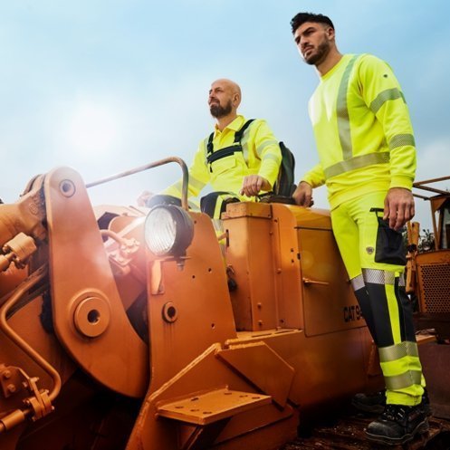 Bauarbeiter in gelber Warnschutzkleidung fahren auf Baumaschine.
