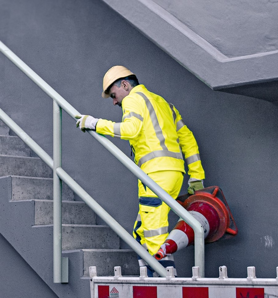 A construction worker wears neon yellow high-visibility clothing and walks up a flight of stairs.