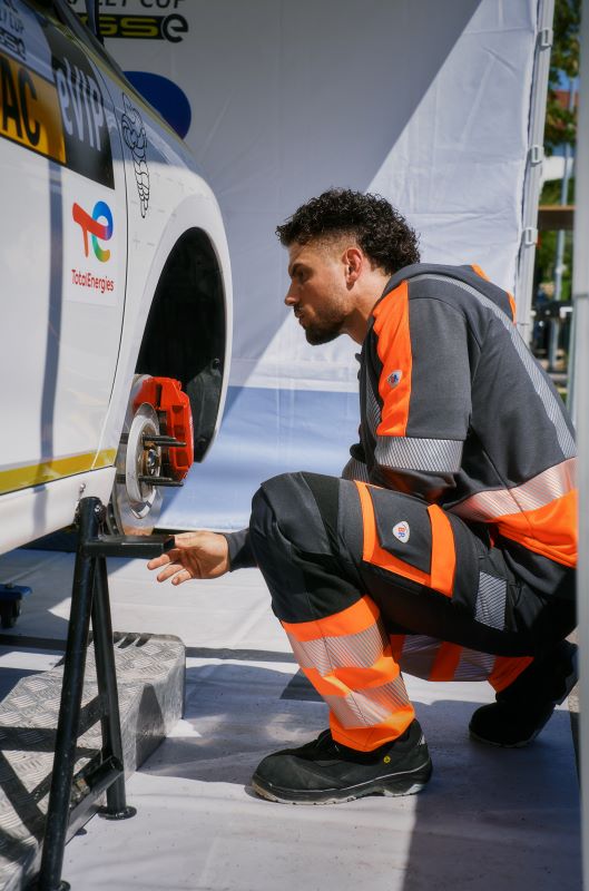 Ein KFZ-Mechaniker kniet bei einem Reifenwechsel in BP® Arbeitskleidung.