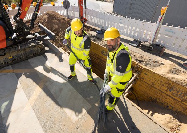 Zwei Bauarbeiter im Strassenbau arbeiten bei Hitze in Arbeitskleidung mit UV-Schutz.