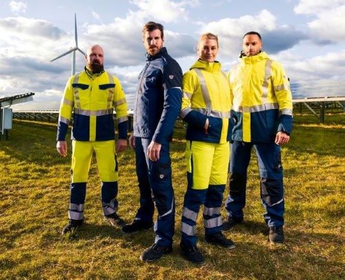 Quatre personnes portant des vêtements de travail modernes à haute visibilité devant des installations d'énergie solaire et éolienne.