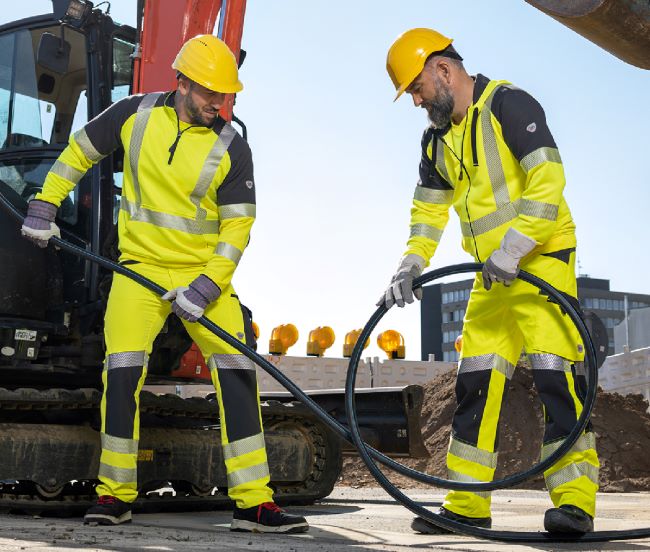 Bauarbeiter in gelber Warnschutzkleidung verlegen Kabel.