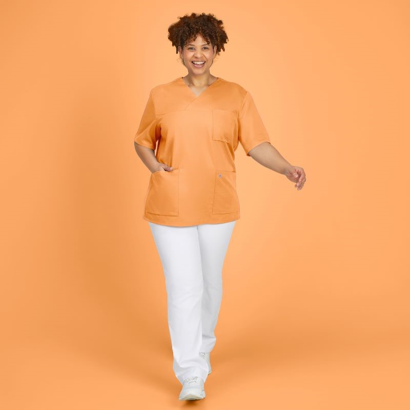 Eine Frau in orangenem Tencel-Kasck und weißer Arzthose vor orangenem Hintergrund.