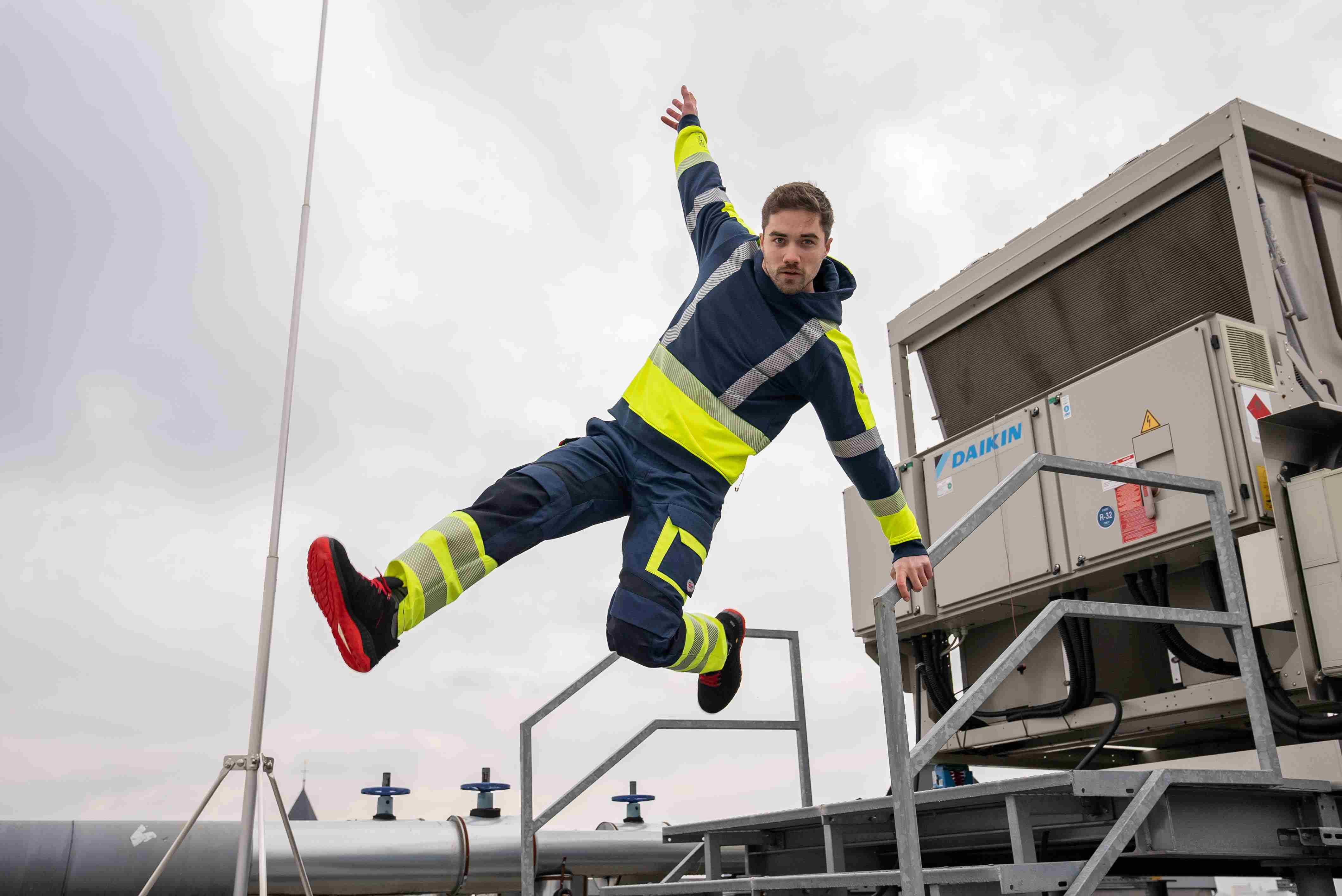 A man jumps down a flight of stairs wearing BP® work clothes in neon yellow.