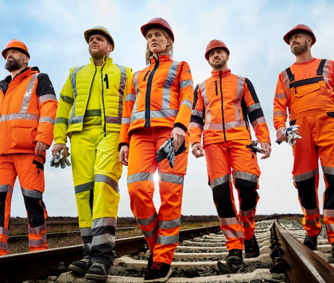Een team van vijf mensen draagt HiVis-kleding op spoorrails.