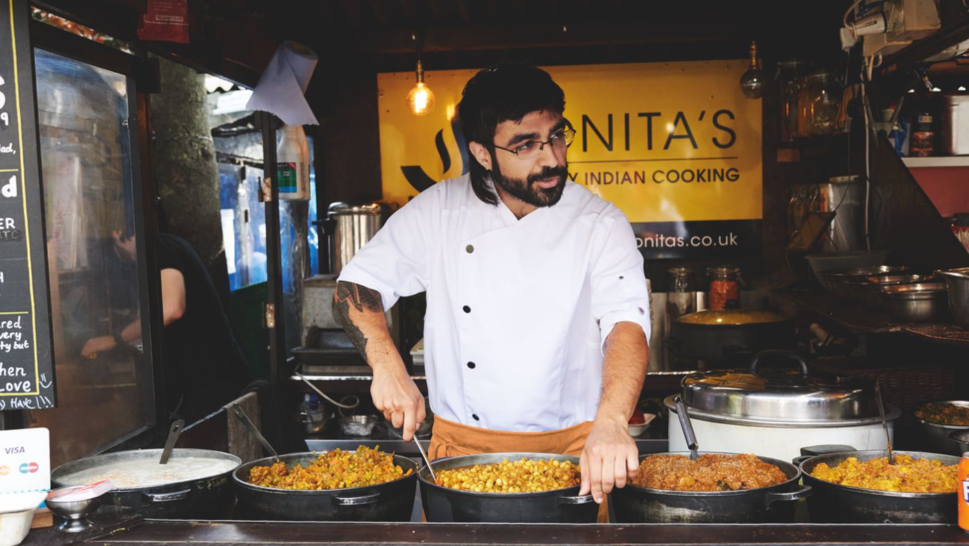 Een mannelijke streetfoodkok draagt een witte koksjas in zijn foodtruck.
