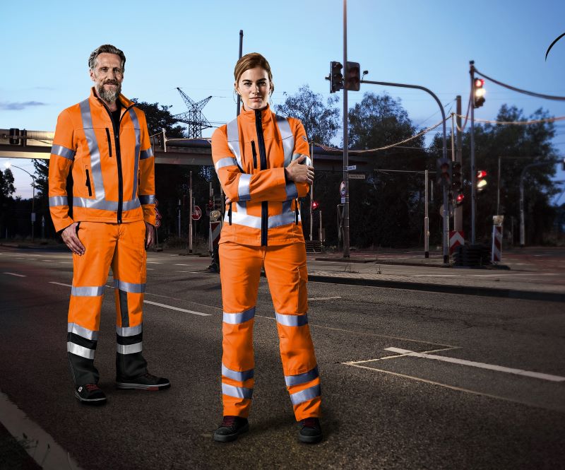 A woman and a man wear orange high-visibility clothing at dusk. 