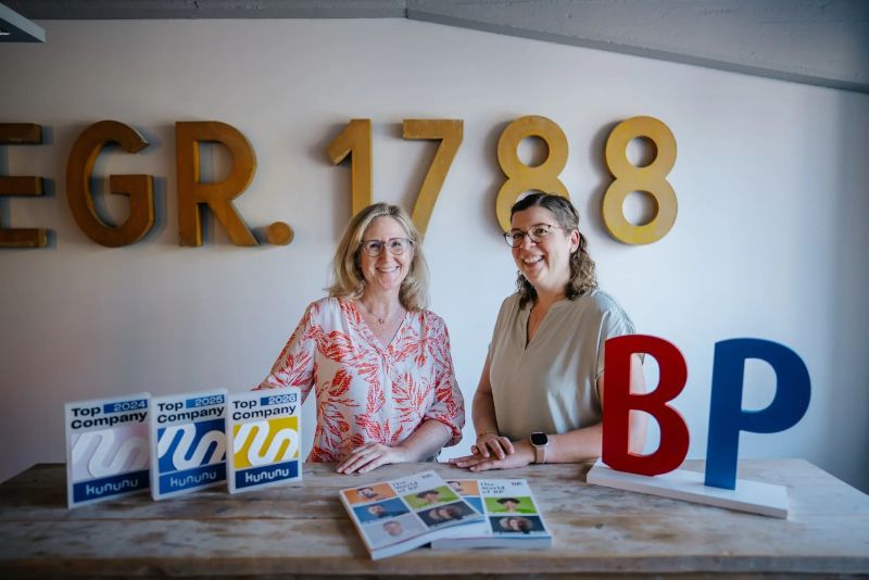 BP® Mitarbeiterinnen im Büro präsentieren Auszeichnungen von kununu.