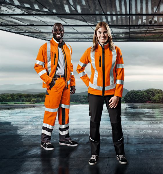 Ein Logistiker und eine Logistikerin posieren in die Kamera und tragen Warnschutzkleidung in orange.