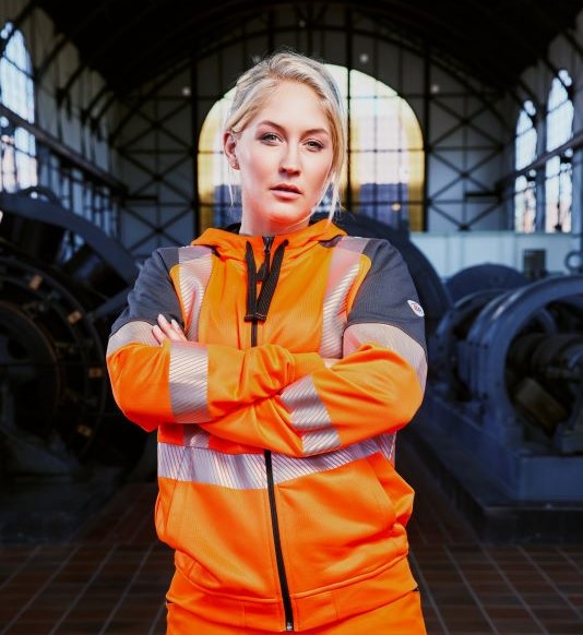 Eine Frau trägt hivis Kleidung für Damen in warnorange.