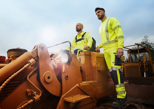 Zwei Bauarbeiter tragen Warnschutzkleidung in neongelb mit UV-Schutz.
