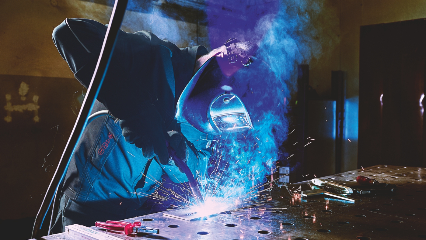 Schweißer in Schutzkleidung schweißt an Eisen.