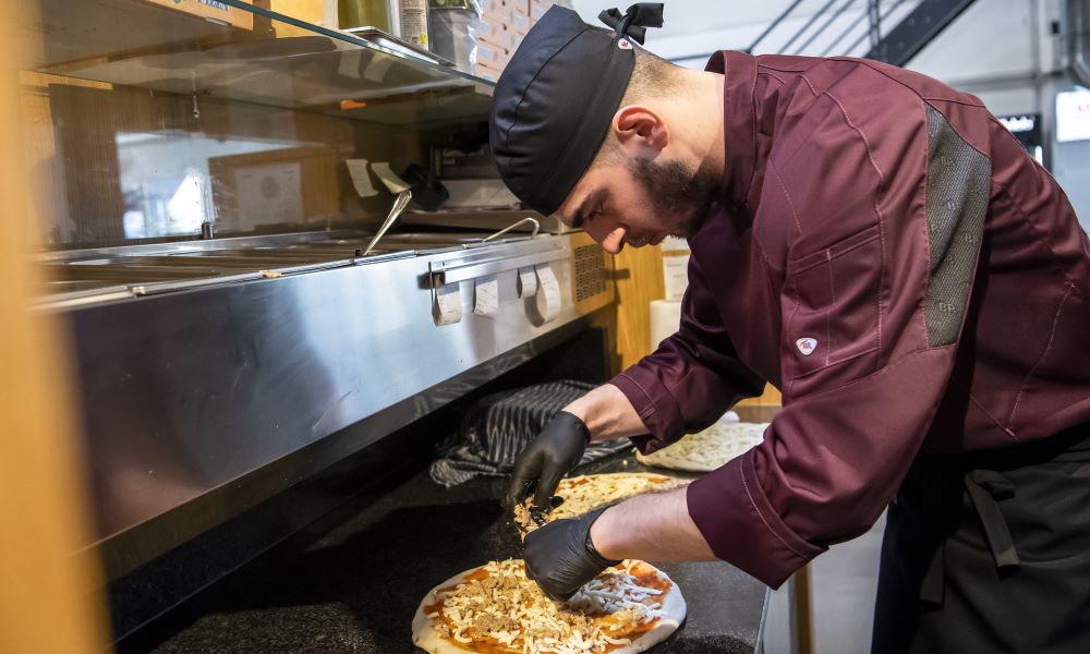 Pizzabäcker in BP Kochkleidung belegt Pizza.