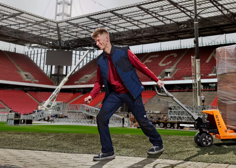 Logistics worker in BP clothing pulls pallet truck through Rheinenergie stadium.