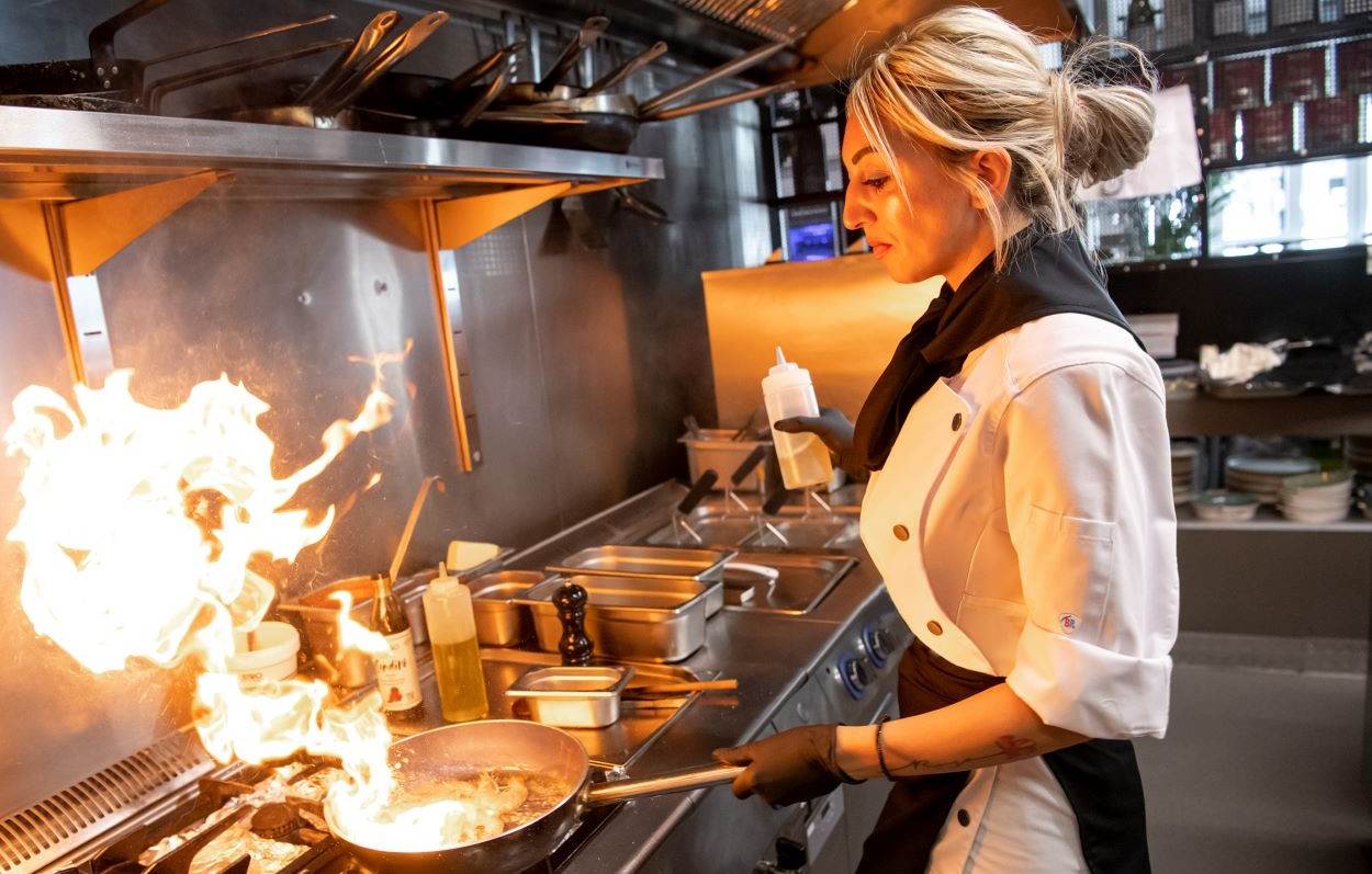 Chefköchin mit weißer Kochjacke ist am Kochen in einer Gastronomie Küche