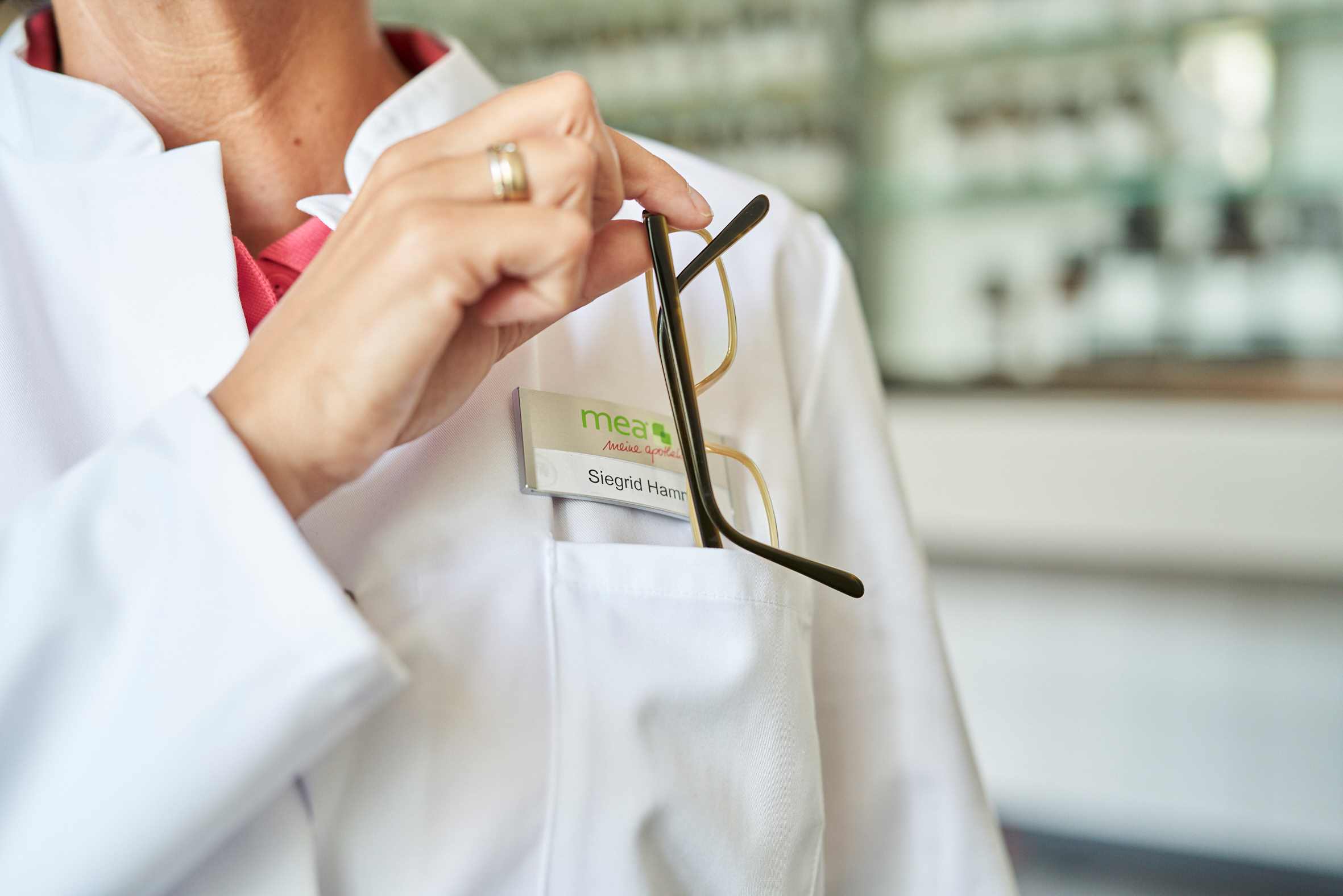 Apothekerin steckt Brille in Brusttasche ihres Arztkittels.