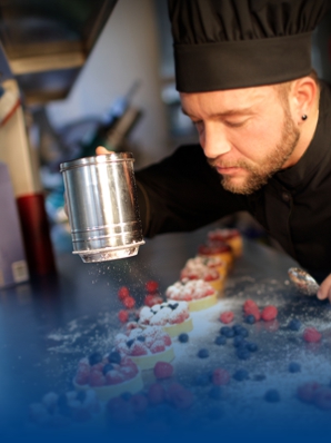 Patissier kantelt poedersuiker en draagt kokskleding.