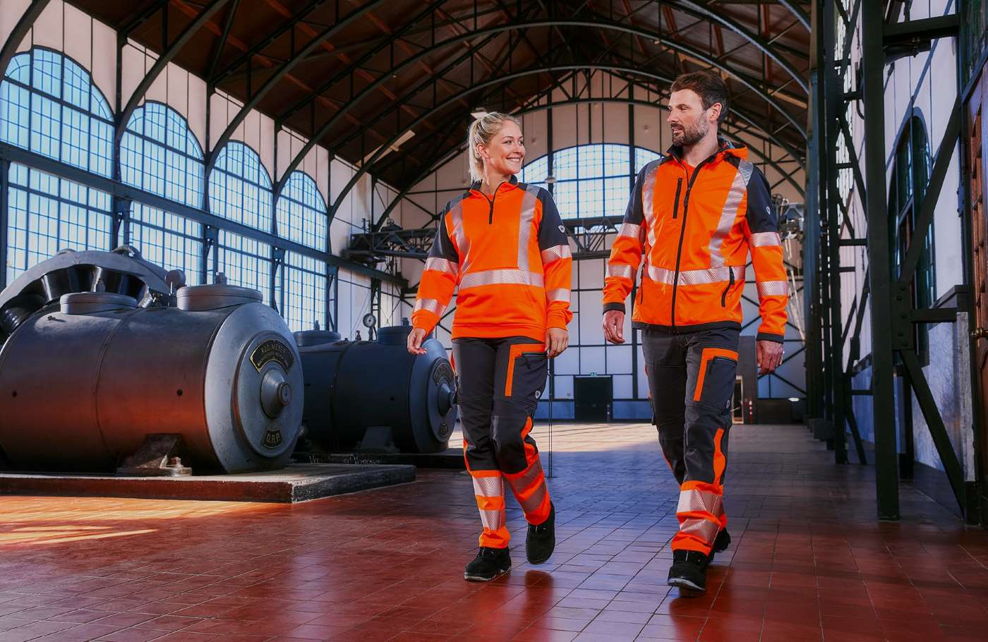 Frau und Mann in Hi-Vis Warnschutzkleidung in Industriehalle.